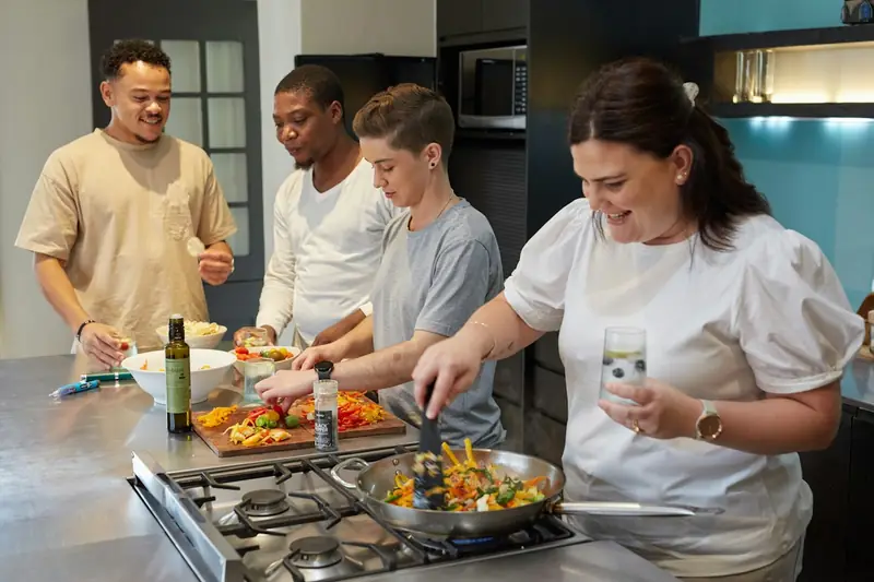 A group cooking together at a cookery class, with a pan of vegetables on the hob.