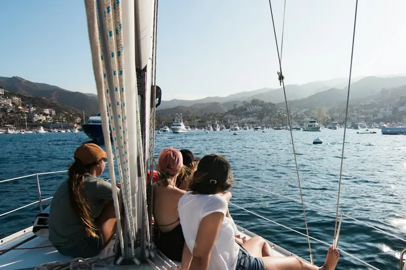 Friends sitting on the bow of a sailing boat in a sunny harbour.