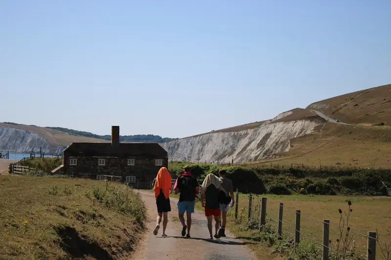 Four walkers with rucksacks on a lane towards a cottage below chalk cliffs.