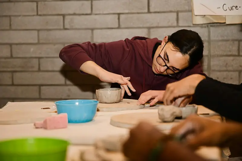 A woman shaping a clay bowl at a shared table in a pottery class.